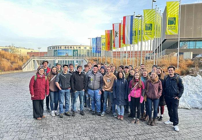 Eine Gruppe von Menschen steht vor einem Großen Gebäude mit der Aufschrift "Messe Berlin". Zu sehen sind auch diverse Fahnen, u.a. Deutschlandfahne, Europafahne sowie einige grüne Fahnen mit der Aufschrift "Grüne Woche".