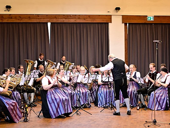 Musikantinnen und Musikanten in Tracht musizieren zusammen. Die Harmoniemusik Hindelang bei der Aufnahme zum Stück "Fast as a Shark".