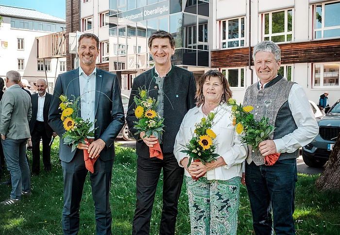Landrat Christian Wilhelm mit seinen Stellvertretern Gerhard Frey, Christine Rietzler und Norbert Meggle. Sie stehen vor dem Gebäude des Landratsamtes Oberallgäu und halten jeder einen kleinen Blumenstrauß in den Händen.
