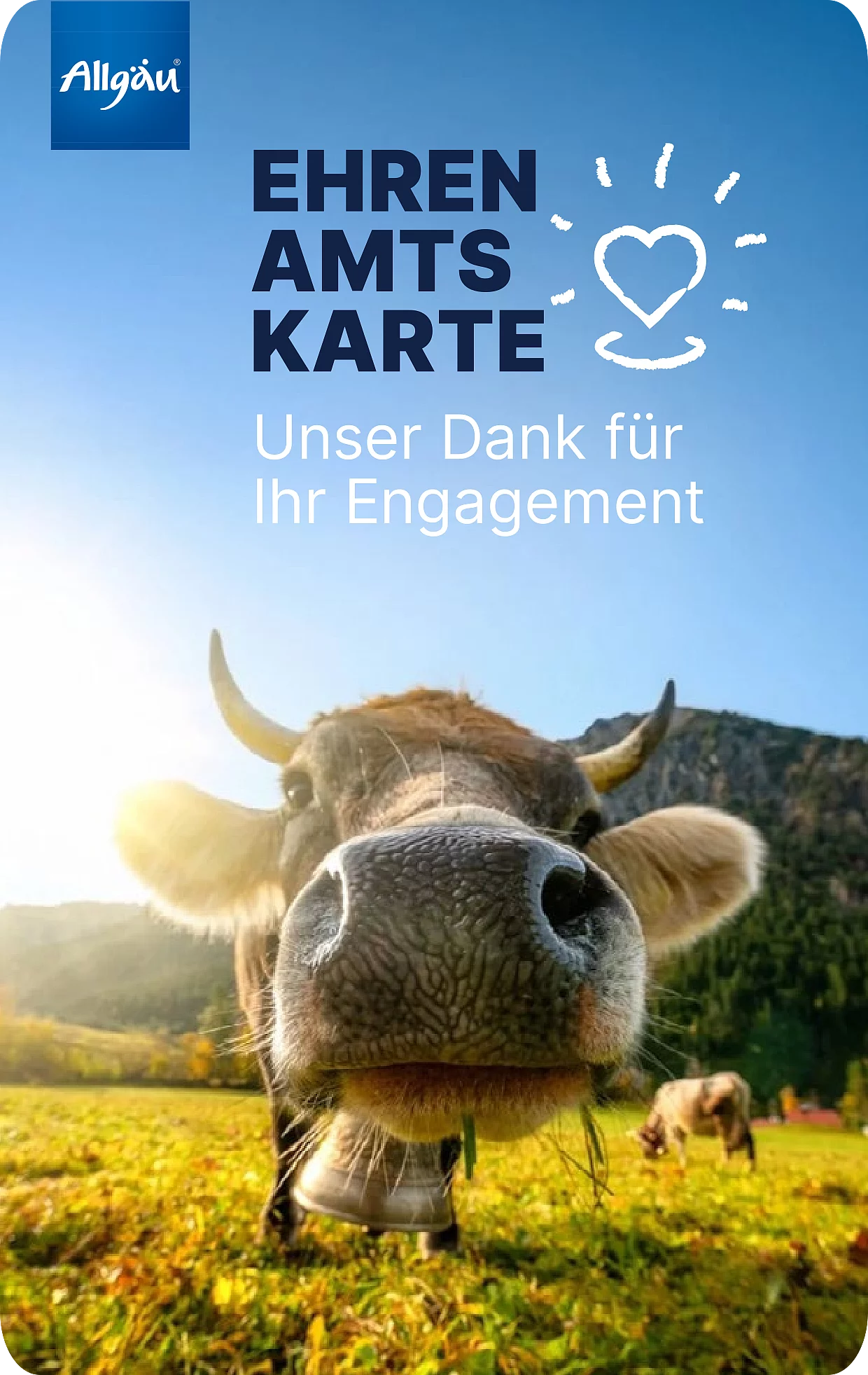 Eine Kuh schaut direkt in die Kamera. Sie steht auf einem grünen Feld. Im Hintergrund sind Berge und der blaue Himmel zu sehen. Das Bild trägt die Aufschrift Ehrenamtskarte - Unser Dank für Ihr Engagement